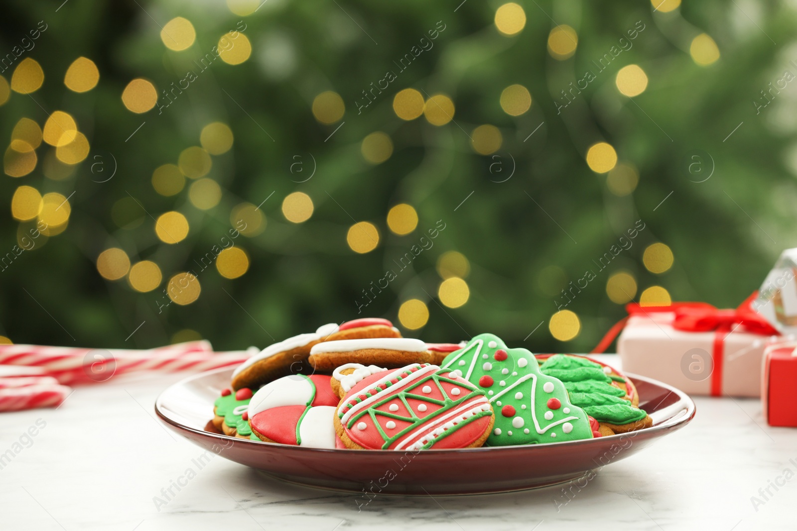 Photo of Decorated cookies on white marble table against blurred Christmas lights