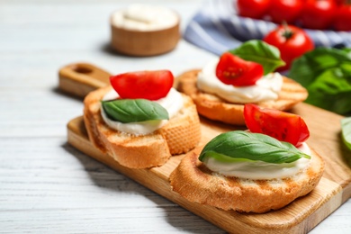 Tasty bruschettas with cheese, basil and tomatoes on white wooden table, closeup