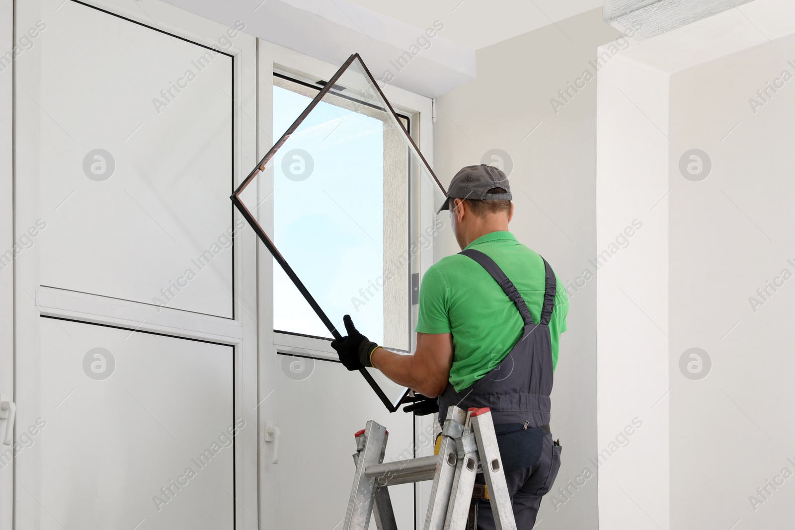 Photo of Worker on folding ladder installing window indoors