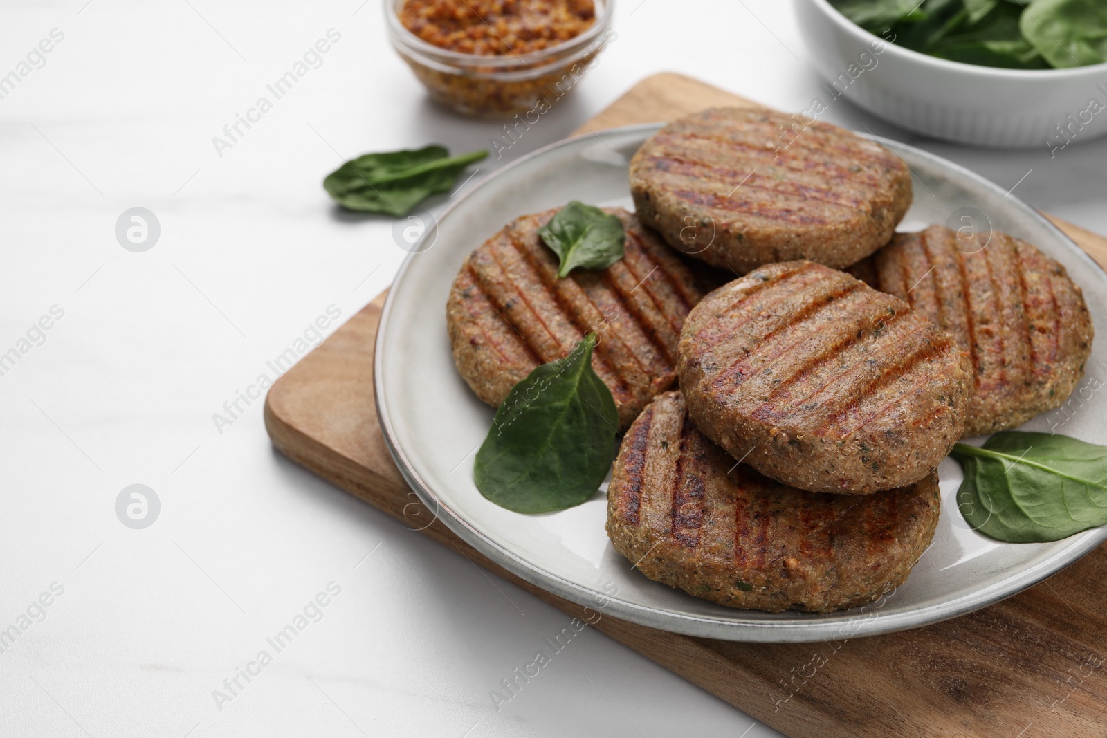 Photo of Tasty grilled vegan cutlets and spinach on white table