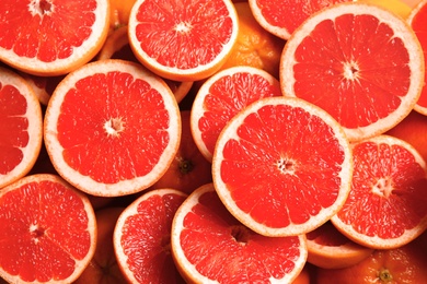 Many sliced fresh grapefruits as background, top view