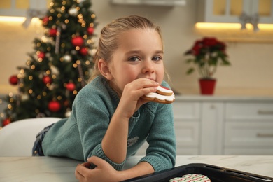 Photo of Cute little girl with freshly baked Christmas gingerbread cookie at table indoors
