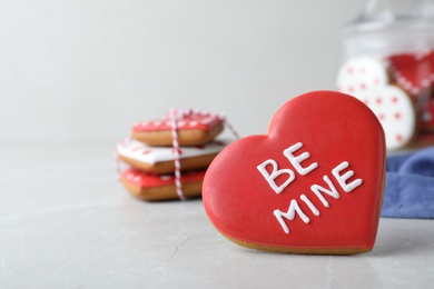 Photo of Delicious heart shaped cookie with phrase Be Mine on light table, space for text. Valentine's Day