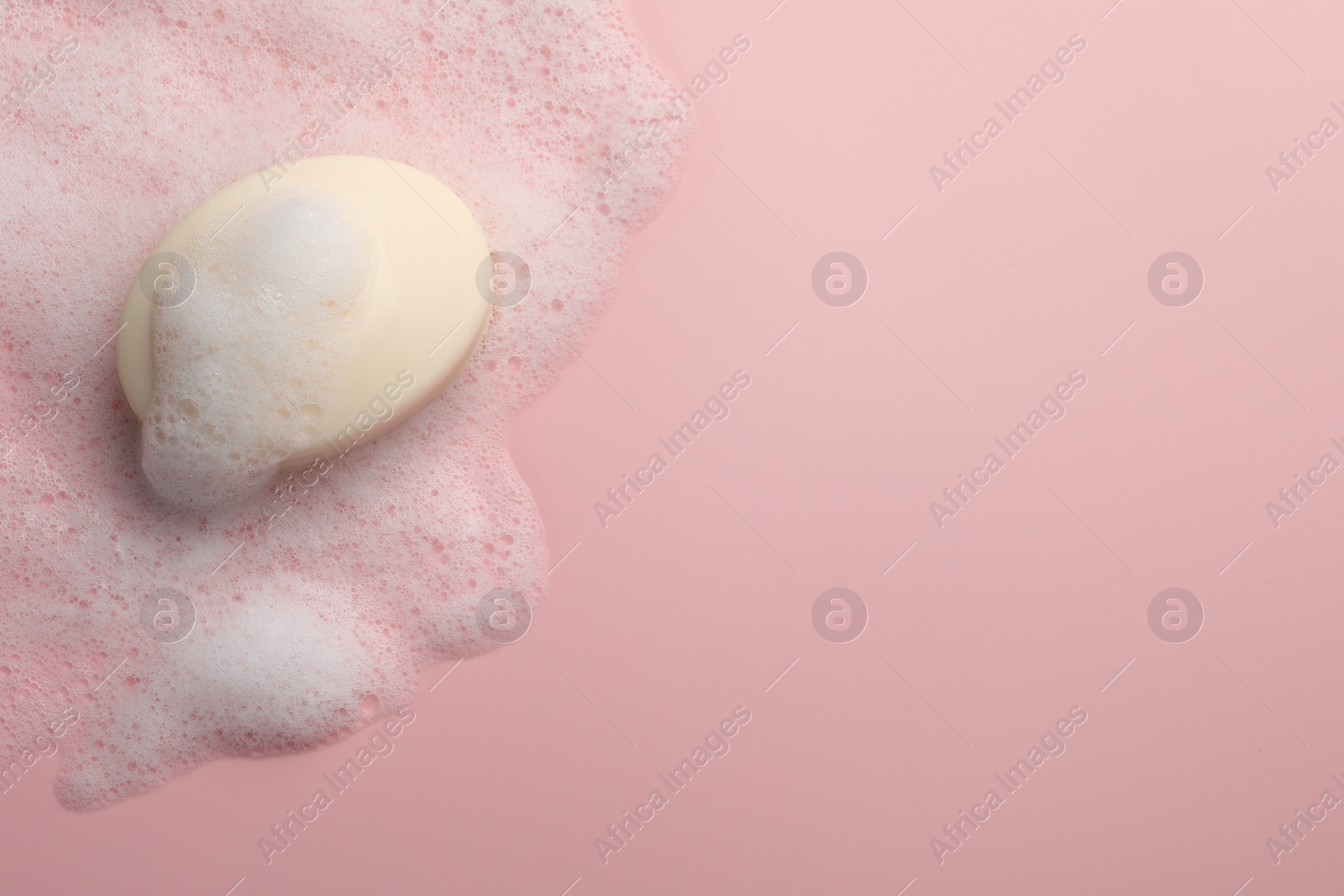 Photo of Soap with fluffy foam on pink background, top view. Space for text