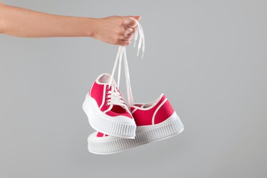 Woman holding pair of classic old school sneakers on light grey background, closeup