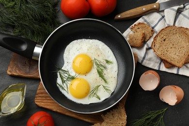 Frying pan with tasty cooked eggs and other products on black table, flat lay