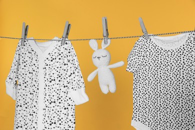 Baby clothes and bunny toy drying on laundry line against orange background, closeup