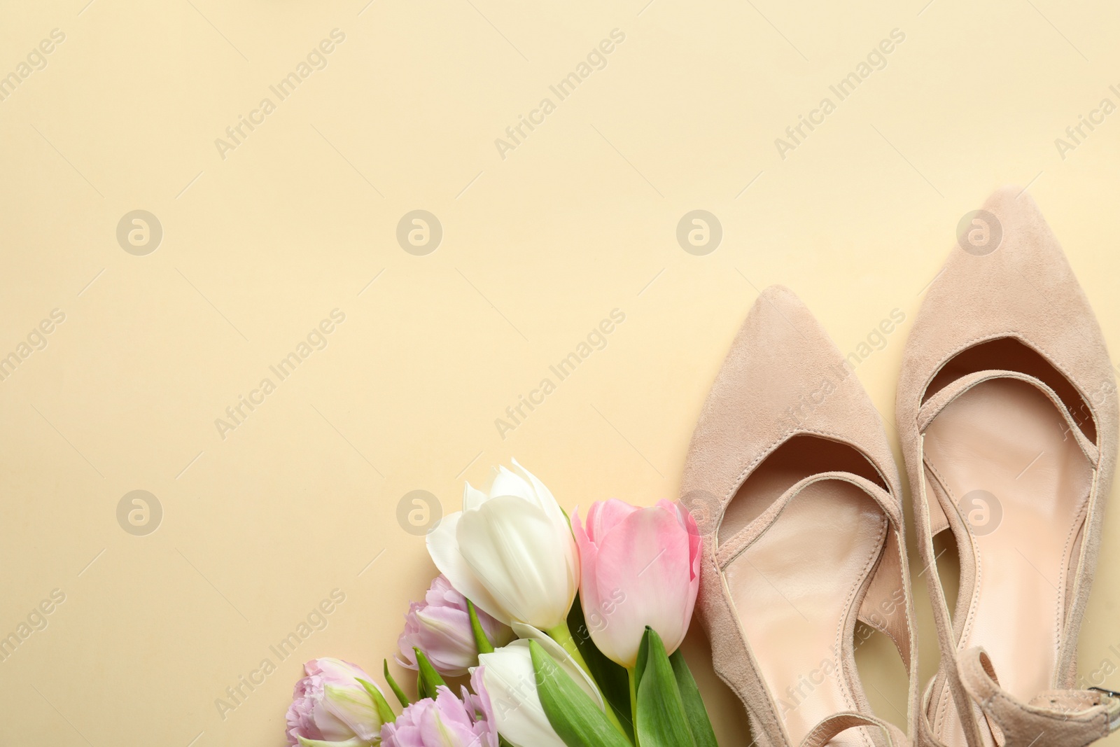 Photo of Stylish shoes and beautiful flowers on beige background, flat lay. Space for text