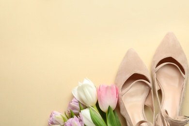 Photo of Stylish shoes and beautiful flowers on beige background, flat lay. Space for text