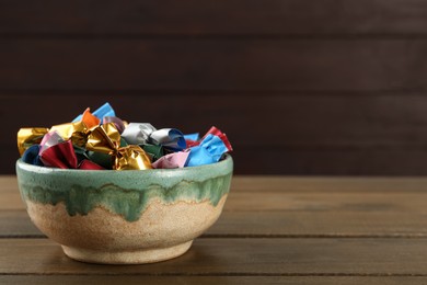 Photo of Candies in colorful wrappers on wooden table, space for text