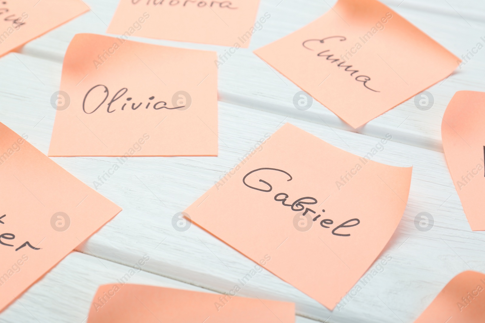 Photo of Paper stickers with different names on white wooden table, closeup. Choosing baby's name