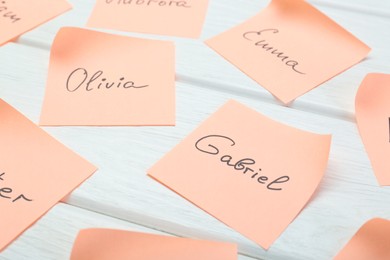 Paper stickers with different names on white wooden table, closeup. Choosing baby's name