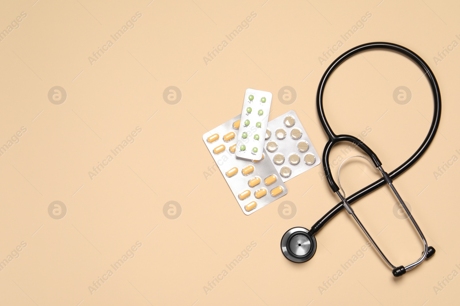 Photo of Stethoscope and pills on beige background, flat lay. Space for text