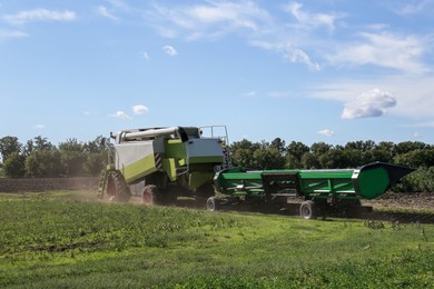 Modern combine harvester with header near agricultural filed