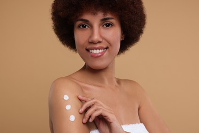 Photo of Beautiful young woman applying body cream onto arm on beige background