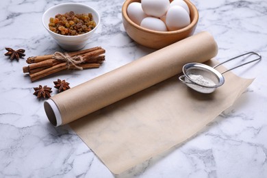 Photo of Roll of baking parchment paper and different ingredients on white marble table