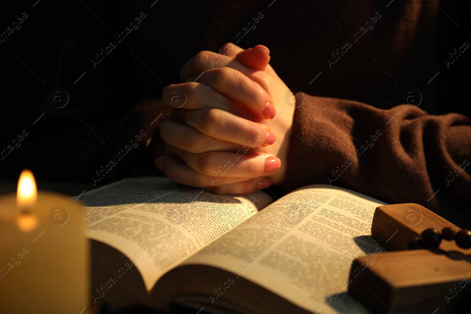 Photo of Woman praying at table with burning candle and Bible, closeup