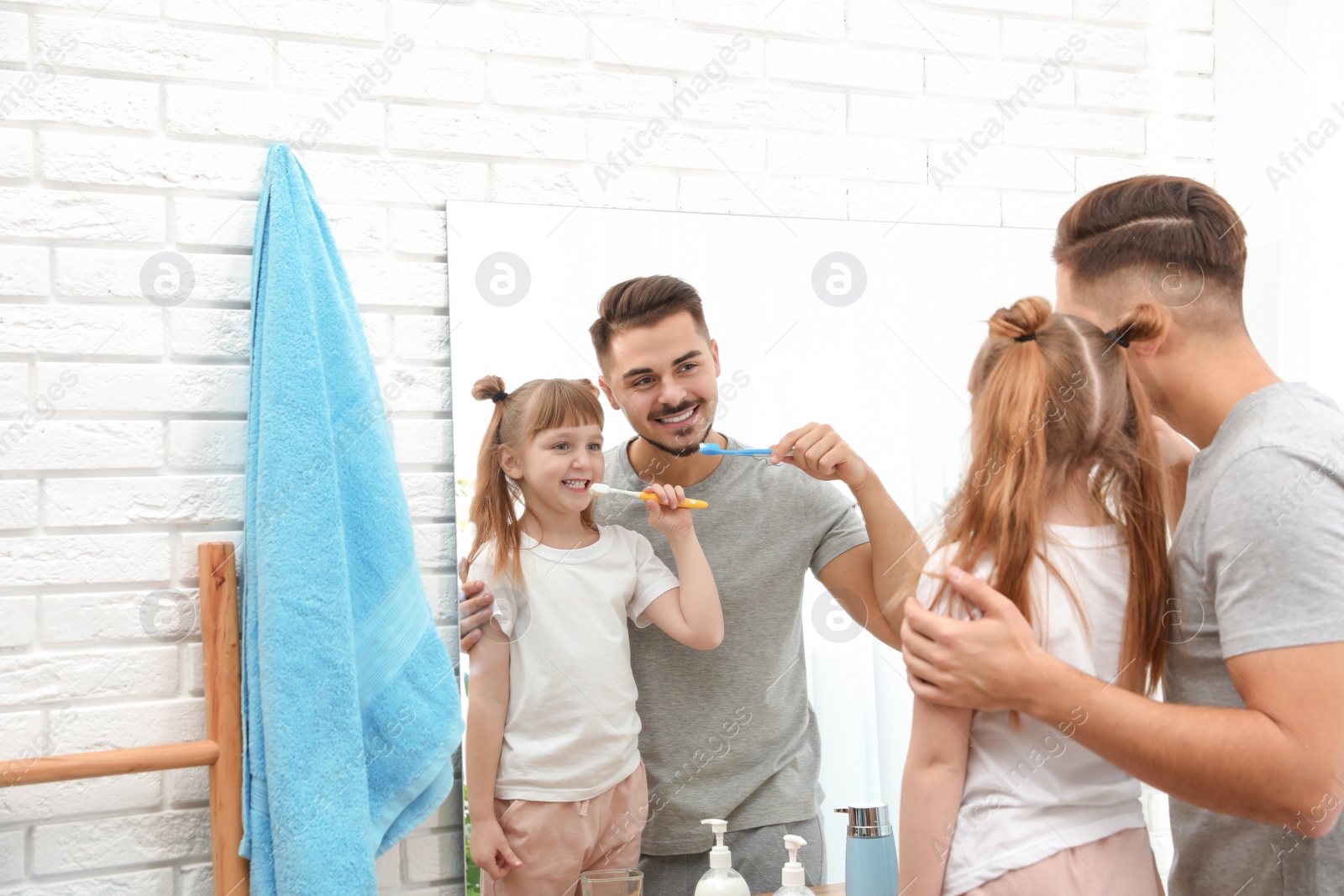 Photo of Little girl and her father brushing teeth together near mirror in bathroom at home. Space for text