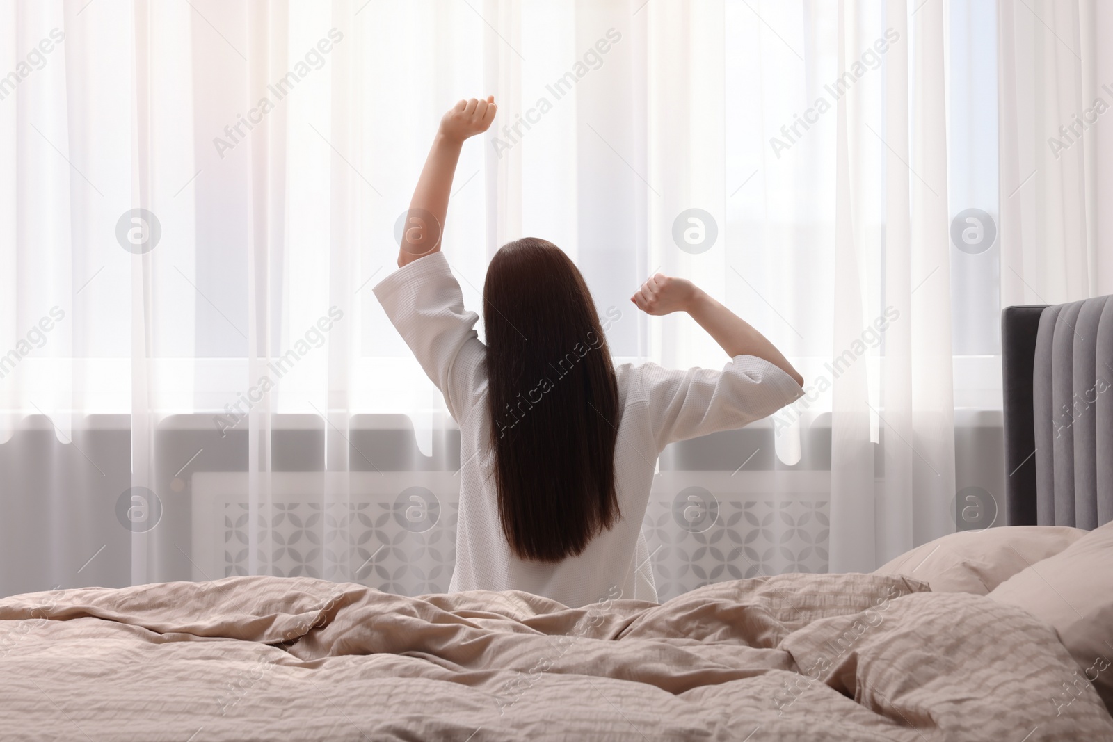 Photo of Woman stretching on bed at home, back view. Lazy morning