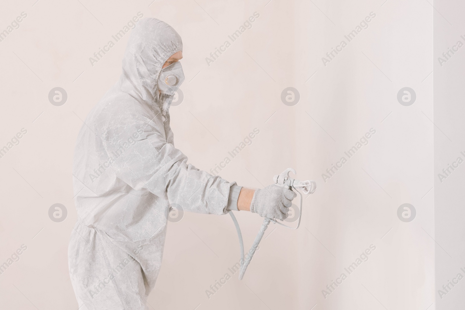 Photo of Decorator in uniform painting wall with sprayer indoors