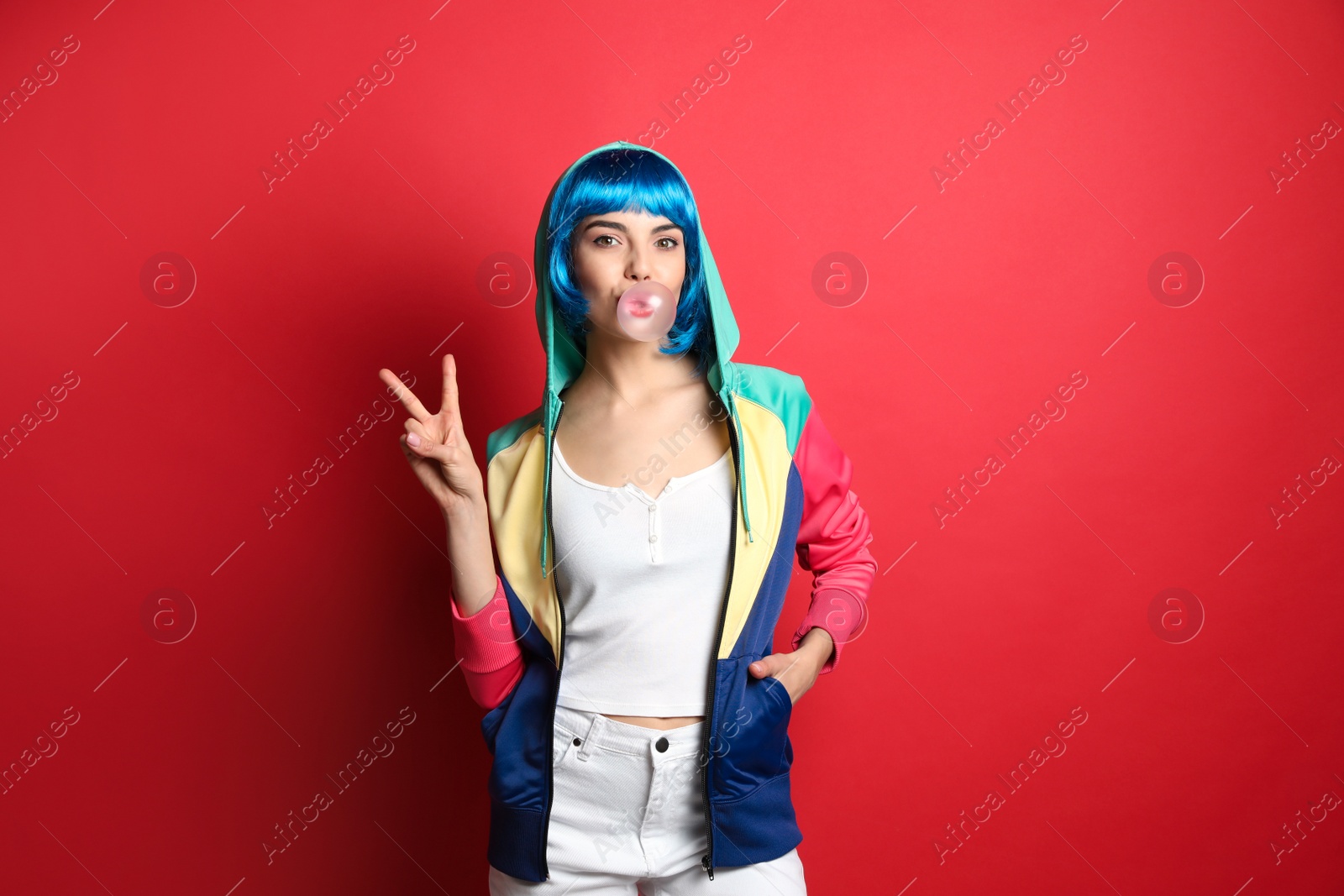 Photo of Fashionable young woman in colorful wig blowing bubblegum on red background