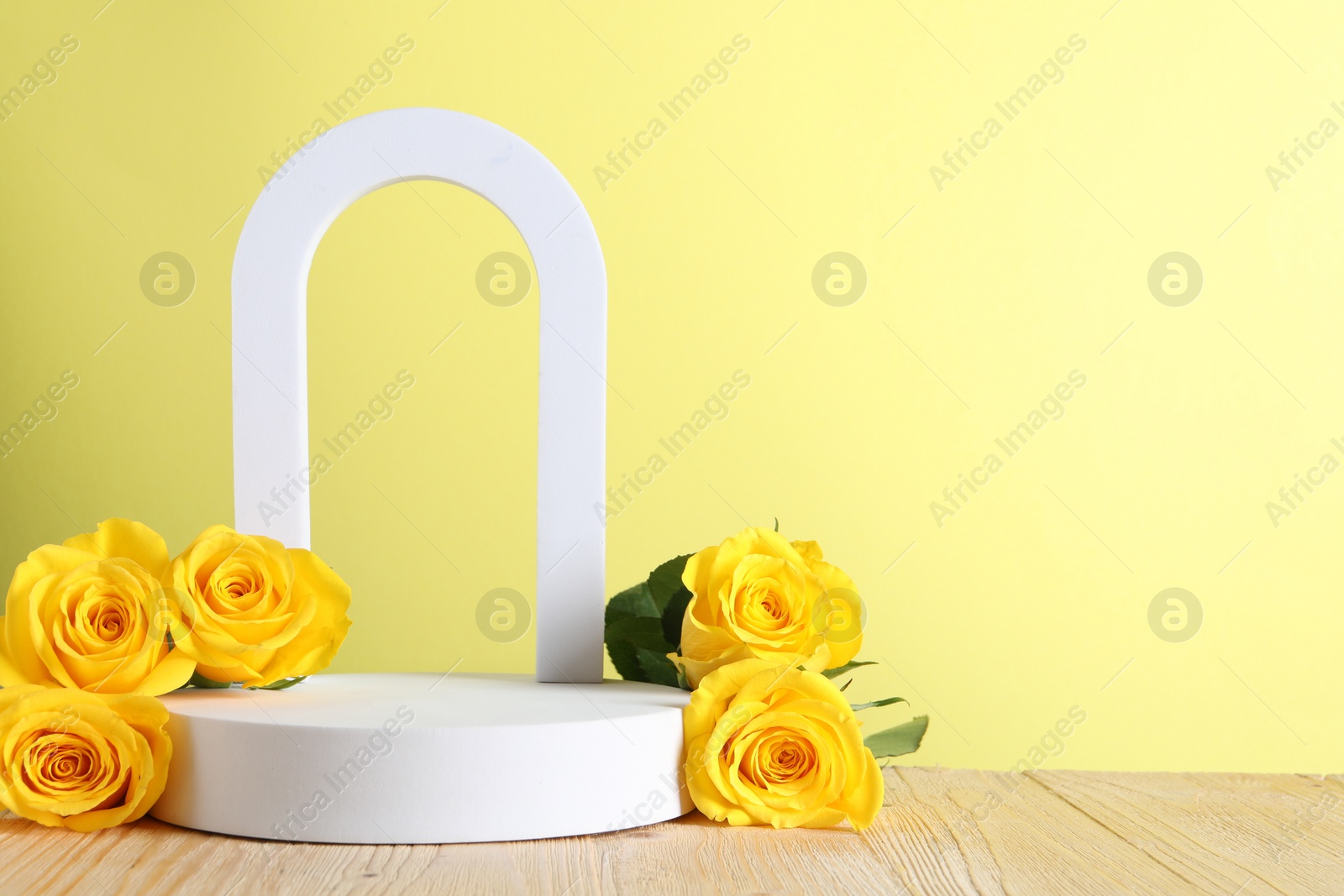 Photo of Beautiful presentation for product. White geometric figures and roses on wooden table against yellow background, space for text