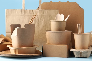 Photo of Eco friendly food packaging. Paper containers, tableware and bag on white table against light blue background