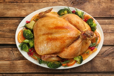 Photo of Roasted chicken with oranges and vegetables on wooden table, top view
