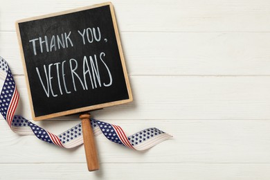 Sign with phrase Thank You, Veterans and ribbon on white wooden table, flat lay. Space for text