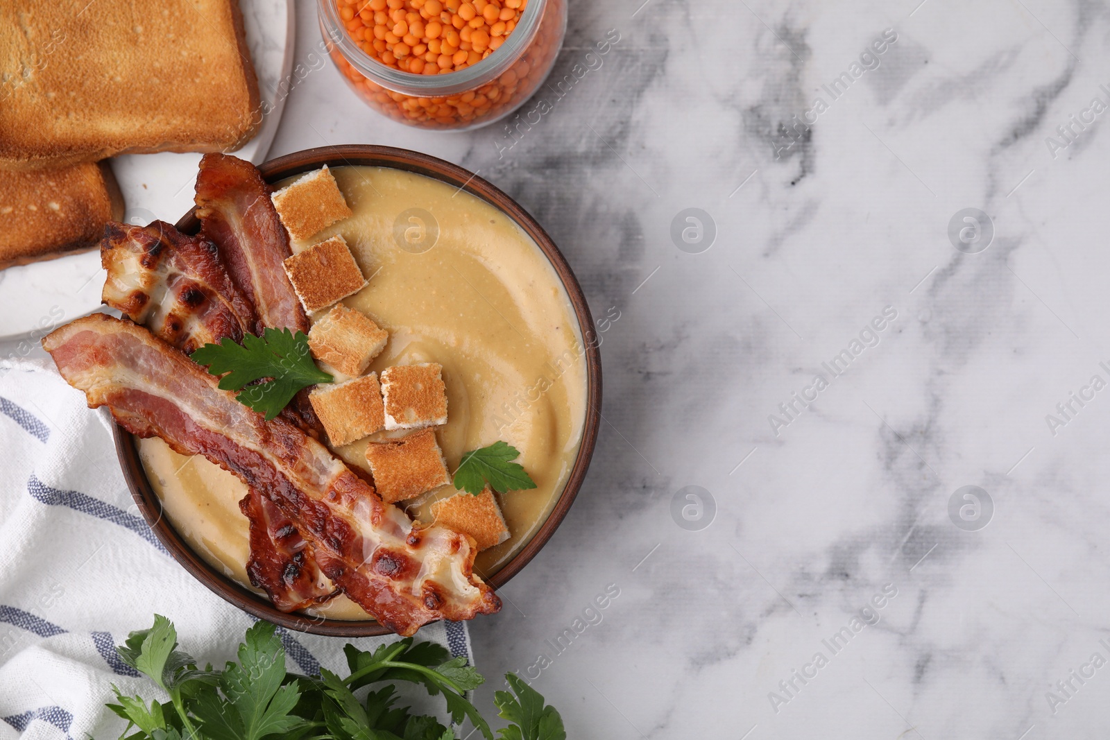 Photo of Delicious lentil soup with bacon and parsley in bowl on light marble table, flat lay. Space for text