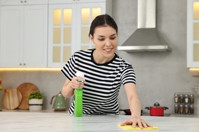 Photo of Woman cleaning countertop with sponge wipe and spray bottle in kitchen