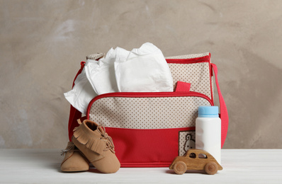 Bag with diapers and baby accessories on white wooden table