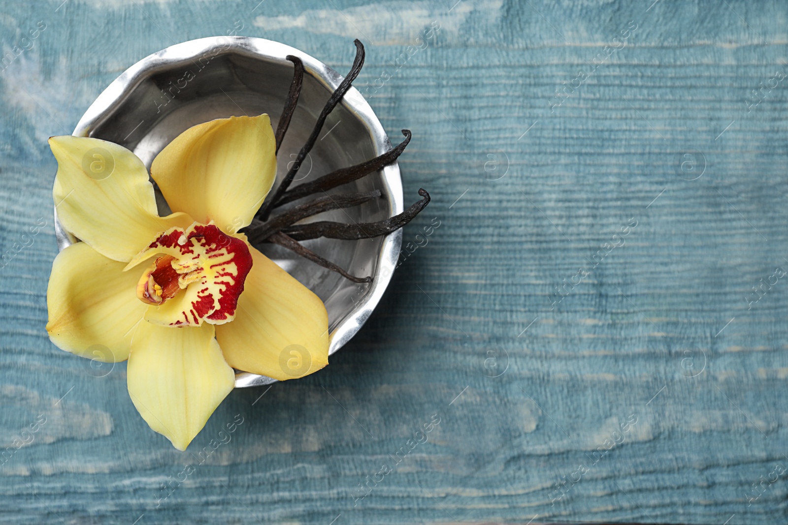 Photo of Bowl with vanilla flower and sticks on wooden background