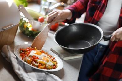 Photo of Woman putting freshly fried eggs with vegetables onto plate in kitchen, closeup