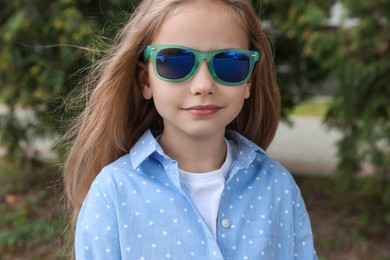 Girl in stylish sunglasses near spruce trees outdoors