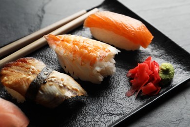 Photo of Serving board with delicious nigiri sushi, ginger and wasabi on black table, closeup