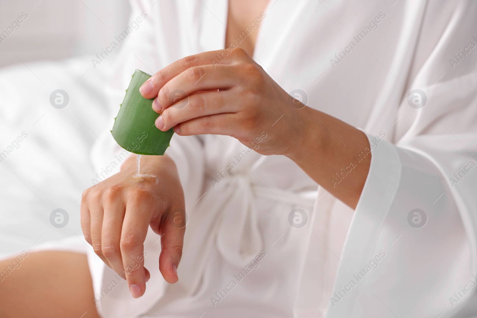 Photo of Young woman applying aloe gel from leaf onto her hand indoors, closeup