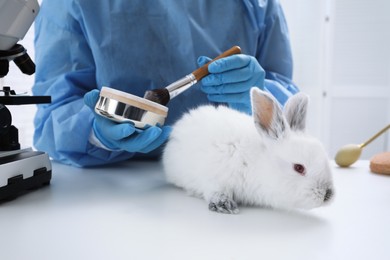 Photo of Scientist with rabbit and makeup products in chemical laboratory, closeup. Animal testing