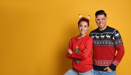 Photo of Couple in Christmas sweaters, Santa headband and party glasses on yellow background, space for text