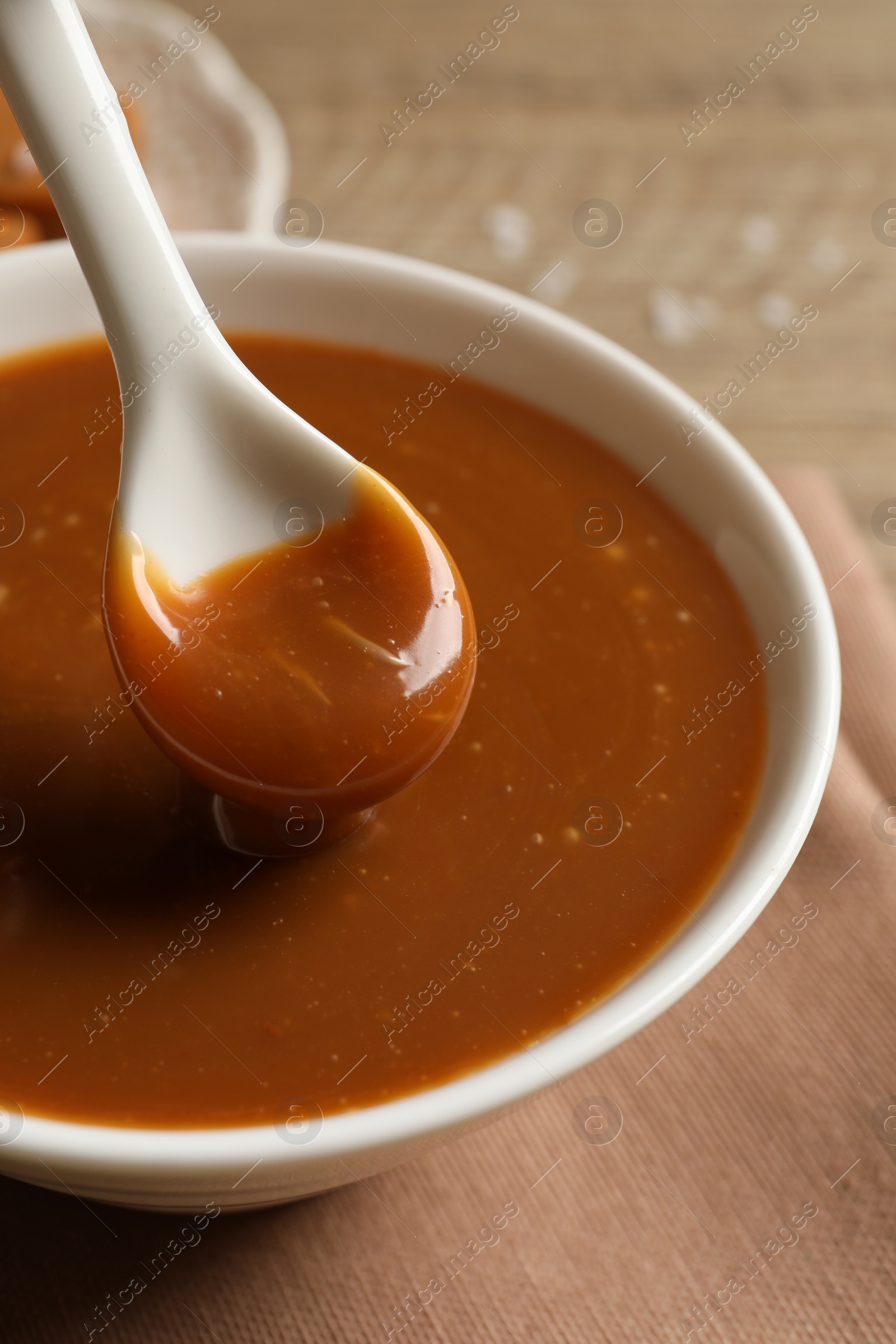 Photo of Taking yummy salted caramel with spoon from bowl at table, closeup