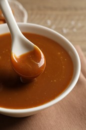 Photo of Taking yummy salted caramel with spoon from bowl at table, closeup