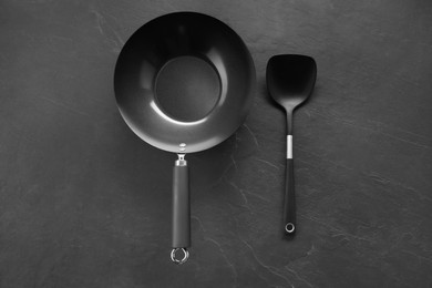 Photo of Black metal wok and spatula on dark textured table, top view