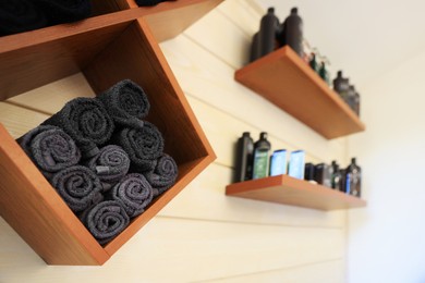 Photo of Shelves with rolled towels and professional hair cosmetics on wall in barbershop, closeup
