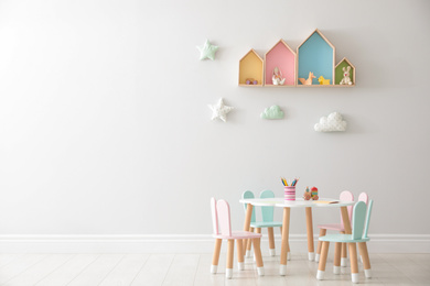 Photo of House shaped shelves and little table with chairs in children's room, space for text. Interior design