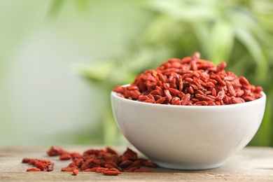 Photo of Bowl of dried goji berries on table against blurred background. Space for text