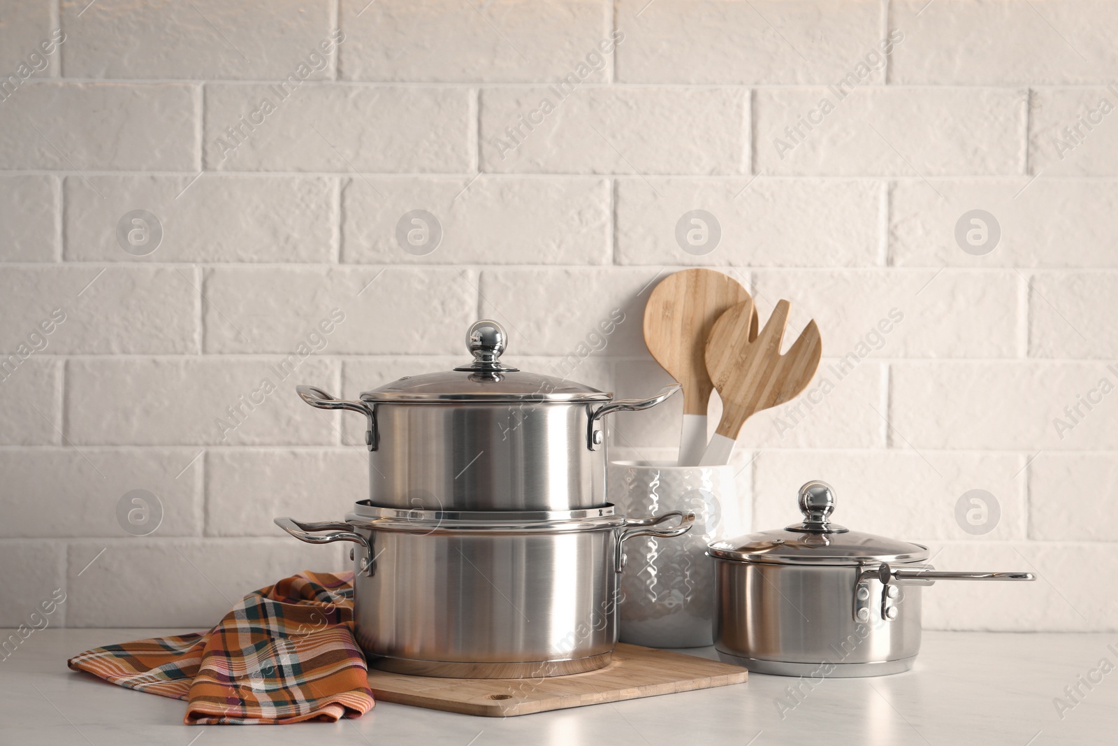 Photo of Set of stainless steel cookware and kitchen utensils on table near white brick wall