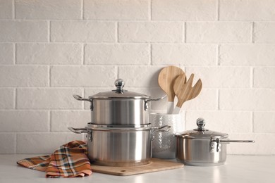 Photo of Set of stainless steel cookware and kitchen utensils on table near white brick wall