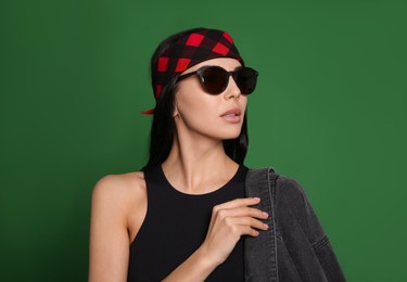 Photo of Fashionable young woman in stylish outfit with bandana on green background