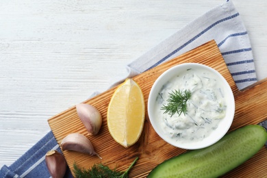 Photo of Tzatziki cucumber sauce and ingredients on wooden background, top view. Space for text