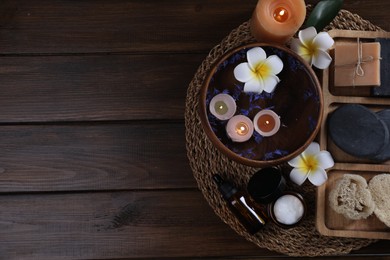 Different spa products, plumeria flowers and burning candles on wooden table, top view. Space for text